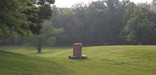 Large rolling swale with stone marker and trees on Santa Fe Trail in Kansas City, Missouri
